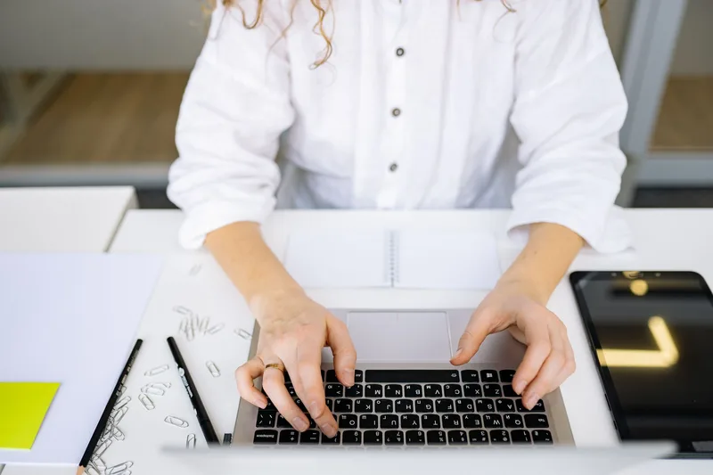 Hands typing actively on a laptop keyboard in a bright modern workspace, representing consistent LinkedIn engagement