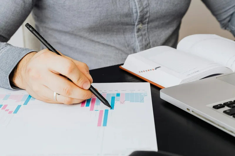 Business analyst reviewing performance data on paper with a laptop nearby, representing LinkedIn personal brand growth tracking