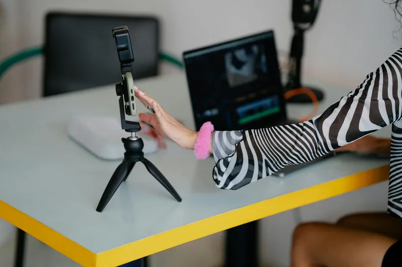 Woman adjusting smartphone on tripod with laptop setup — TikTok content ideas for digital product sellers
