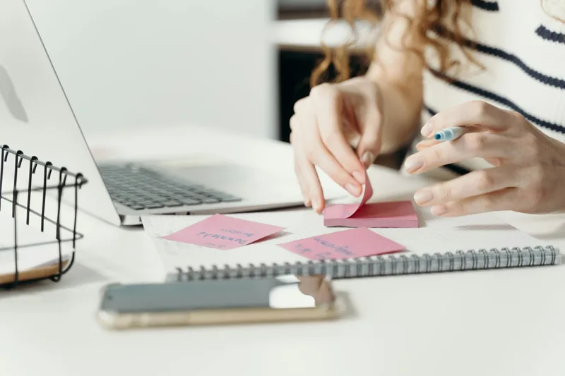 Woman organizing content notes with a laptop and smartphone at a modern workspace